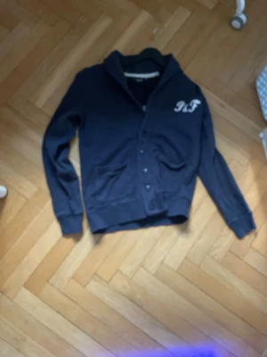 Svart hoodie från Pinefield Selection - Snygg blå hoodie från Pinefield Selection med tryck både fram och bak. Hoodien har knäppning framtill, två fickor. Pris kan diskuteras.