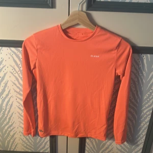 Orange långärmad tröja från Olaian - Säljer en snygg orange långärmad tröja från Olaian. Tröjan har en enkel och sportig design med rund halsringning och är tillverkad i ett mjukt syntetmaterial som passar perfekt för aktiva dagar.