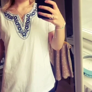Vit blus med blå broderier - Säljer en vit blus med korta ärmar och snyggt blått broderi runt den v-ringade halsen. Blusen har en luftig passform och är perfekt för varmare dagar. Broderierna ger en bohemisk och unik touch till outfiten. Köpte i Spanien använt typ 2 ggr men tröttnar väldigt fort på kläder