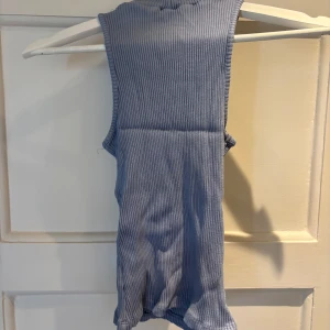 Blå ribbad polotopp från NA-KD - Säljer en ljusblå ribbad polotopp från NA-KD. Toppen är ärmlös med hög krage och har en tight passform. 