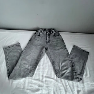 Gråa jeans  - Säljer ett par gråa jeans med raka ben och hög midja. Jeansen har klassisk femficksdesign, bälteshällor och är tillverkade i ett mjukt denimtyg. Perfekt för alla årstider!