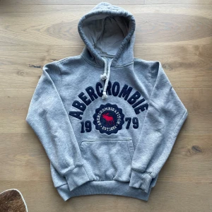 Grå hoodie från Abercrombie & Fitch - Stilren grå hoodie från Abercrombie & Fitch. Har en ytterst liten defekt på kragen som knappt syns. Tröjan har storlek M men passar med XS/S. Pris är diskuterbart och hör av er vid minsta fundering! Ps: kragen är fixad!!
