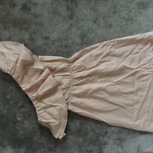 Beige offshoulder långklänning - Säljer en beige långklänning med offshoulder-modell och volangdetalj upptill. Klänningen har resår i midjan för en snygg passform och är tillverkad i ett lätt tyg, perfekt för varmare dagar. Enkel och stilren design som känns både trendig och romantisk.