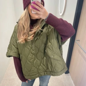 Olivgrön quiltad jacka - Säljer denna jätte snygga och eftertraktade olivgröna quiltade jackan/cape med korta ärmar och dragkedja framtill! Perfekt för lager på lager stil. As snygg oversized passform