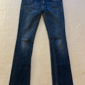 Miss Me blå bootcut jeans med brodyr - Snygga blå jeans från Miss Me med bootcut passform och broderade bakfickor med glittriga detaljer. Jeansen har låg midja, slitna detaljer vid benslut och kontrastsömmar. Perfekta för dig som gillar en unik och trendig look. 