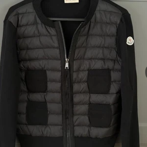 Svart moncler cardigan dam - Svart cardigan jacka från Moncler med quiltad framsida i syntet och stickade ärmar. Fyra framfickor, rund hals och dragkedja framtill. Klassisk Moncler-logga på ärmen. Perfekt för dig som gillar stilren och sportig look, säljer min flickväns cardigan, order bekräftelse samt bevis på äkthet finns!
