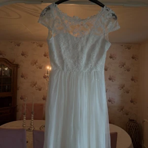 Vit långklänning med spets från Vila - Superfin vit långklänning från Vila med spets upptill och vackra knappar i ryggen. Klänningen har korta ärmar, rund halsringning och ett flowy kjolparti i tunt tyg. Perfekt för dig som vill ha en romantisk och elegant look.