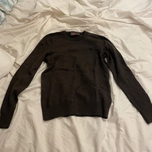 Mörkbrun merinoullströja Morris XS - Säljer en mörkbrun, klassisk rundhalsad tröja från Morris i 100% merinoull. Tröjan har lång ärm, ribbade muddar och en diskret broderad logga på bröstet. Perfekt för dig som gillar stilrena och bekväma plagg.