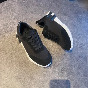 Svarta sneakers med vit sula - Säljer ett par svarta sneakers med chunky vit sula och coola detaljer på hälen. Skorna har snörning och är gjorda i en mix av mocka och syntetmaterial. Perfekta för dig som gillar en sportig och modern look.