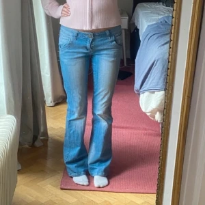 Lågmidjade bootcut jeans - Snygga ljusblå lågmidjade bootcut jeans från C-NIC med låg midja och coola dragkedjedetaljer på bakfickorna. Jeansen har klassisk femficksdesign och är tillverkade i mjukt denimtyg. Perfekta för dig som gillar en avslappnad men trendig look.