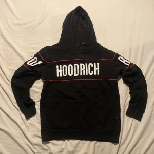 Svart hoodie från Hoodrich  - Svart hoodie från Hoodrich i storlek medium med stor vit logga på bröstet och armarna. Hoodien har röda detaljer, huva och en stor magficka. Perfekt för dig som gillar streetwear och vill sticka ut med en fet logga.
