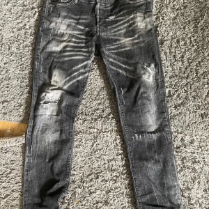 Dsquared2 - Säljer ett par svarta jeans från Dsquared2 med coola slitningar och distressed detaljer. Jeansen har smal passform och klassisk femficksdesign. Tillverkade i Italien och gjorda i stretchig bomull för extra komfort. Perfekta för dig som gillar en edgy streetstil.