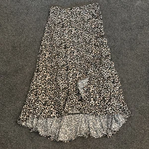 Leopardmönstrad långkjol med volang - Säljer en snygg långkjol med leopardmönster i svart och beige. Kjolen har en lätt volangkant nedtill och är tillverkad i ett tunt, flowy material som ger en skön känsla. 