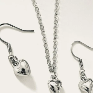 Smyckeset med hjärtan i silverfärg halsband 45 cm längd - Snyggt smyckeset med halsband och örhängen i silverfärg. Både halsbandet och örhängena har blanka hjärtformade hängen som ger en söt och trendig look. Perfekt för dig som gillar stilrena accessoarer med en romantisk touch.