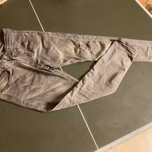 Grå Lee jeans med slitning - Säljer ett par grå jeans från Lee med snygg slitning på ena benet. Jeansen har klassisk femficksdesign, smal passform och är tillverkade i mjukt bomullsmaterial. Perfekta för dig som gillar en avslappnad men ändå stilren look.