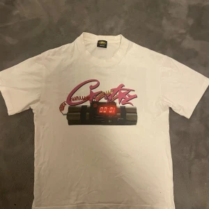 Corteiz No Time 4 Luv - Vit t-shirt från Corteiz storlek medium med tryck av en digital bomb och graffiti-inspirerade text på framsidan. Baksidan har ett stort svart tryck med texten 'NO TIME 4 LUV'. Klassisk rund hals och korta ärmar. Materialet är mjuk bomull.