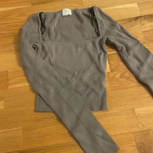 Grå ribbad långärmad topp - Säljer en stilren grå ribbad topp med lång ärm och fyrkantig halsringning. Toppen har en tight passform och är perfekt att matcha med både jeans och kjol. Materialet är mjukt och stretchigt 