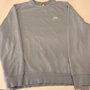 Ljusblå Nike sweatshirt i fleece M - Ljusblå sweatshirt från Nike med broderad vit logga på bröstet. Tröjan har rund hals, långa ärmar och är fodrad med mjuk fleece på insidan. Perfekt för kalla dagar och sportig stil.