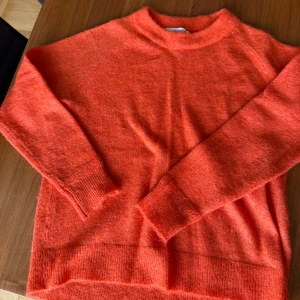 Orange stickad tröja från Selected Femme - Supermjuk och fluffig orange stickad tröja från Selected Femme. Tröjan har rund hals, långa ärmar och breda ribbade muddar vid ärmslut och nederkant. Perfekt för lager-på-lager och ger en färgklick till din outfit.