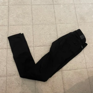 Svarta Replay Hyperflex jeans - Svarta Replay Hyperflex jeans med klassisk femficksdesign och smal passform. Stretchigt material som ger extra komfort och rörelsefrihet. Perfekta för dig som vill ha ett par stilrena och bekväma jeans med modern känsla.