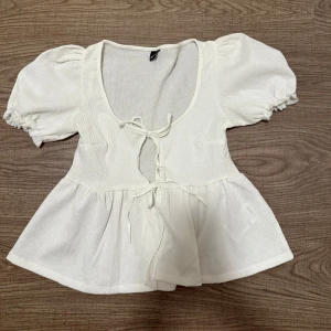 Vit blus  - Supersöt vit blus från Gina Tricot med puffiga korta ärmar och två knyt framtill. Har aldrig användt den då jag känner att den inte passar mig så helt ny. Den är i storlek xs.