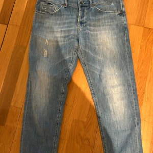 Ljusblå jeans med slitningar dondup george - Säljer ett par ljusblå jeans med snygga slitningar och klassisk femficksdesign. Jeansen har raka ben och orangea sömmar på bakfickan. Perfekta för en avslappnad och trendig look.