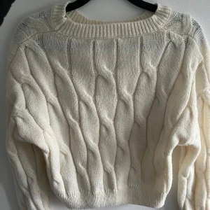 Vit kabelstickad tröja - Säljer en vit kabelstickad tröja med grova flätmönster och rund hals. Tröjan har lång ärm och ribbade muddar vid hals, ärmslut och nederkant. Perfekt för dig som gillar en mysig och stilren look under kyliga dagar.