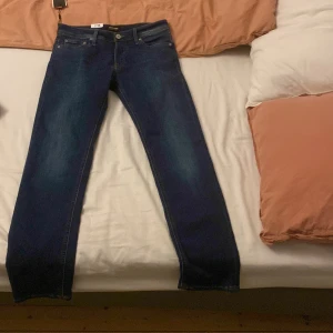 Slim Glenn blå jeans från Jack & Jones - Mörkblå jeans från Jack & Jones, modell Slim Glenn. Snygg slim fit med klassisk femficksdesign och subtila slitningar framtill. Jeansen har normal midja och är tillverkade i stretchig bomullsdenim för skön passform.