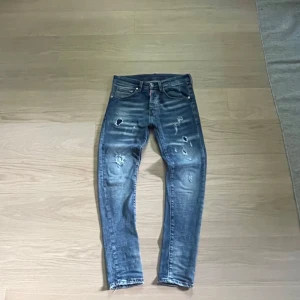 Dsqaured2 jeans med slitningar - Säljer ett par ljusblåa Dsquared2 jeans med snygga slitningar framtill. Lite lagade vid skrevet men det är fixat och det håller, man ser de inte ens.