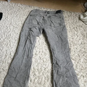 Grå bootcut jeans i denim - Säljer ett par grå jeans med bootcut-modell och klassisk femficksdesign. Jeansen har en snygg tvättad look och är tillverkade i denim. Passar dig som gillar en avslappnad men ändå trendig stil. Men även dom som har storlek M kan ha dom