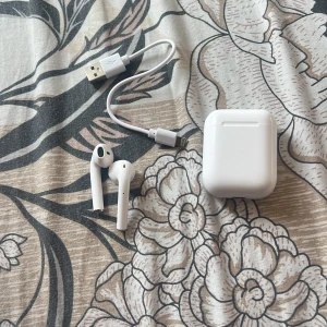 AirPods (2nd generation) - Säljer ett par Apple AirPods (2nd gen) med laddningsetui och laddkabel. Hörlurarna är i fint skick utan synliga repor eller skador. Perfekt för trådlös musik och samtal. Fungerar utmärkt och är redo att användas direkt.