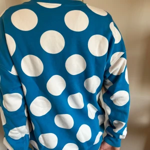 Blå prickig tröja från Moschino - Säljer en blå sweatshirt från Moschino med stora vita prickar och svart logga framtill. Tröjan har rund hals, långa ärmar och är gjord i mjuk bomull. Perfekt statement-plagg för dig som gillar färg och mönster!