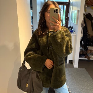 Olivgrön teddyjacka med knappar - Säljer en olivgrön teddyjacka med oversized passform och stora knappar framtill. Jackan har två fickor och är gjord i ett mjukt, fluffigt material som känns riktigt cozy. Perfekt för dig som vill ha en chill och trendig look i höst och vinter.