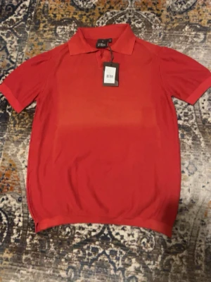 Röd pikétröja från Oscar Jacobson - Säljer en röd pikétröja från Oscar Jacobson i storlek M. Tröjan har klassisk krage, korta ärmar och diskret struktur i tyget. Perfekt för dig som gillar stilrena och tidlösa plagg. Märkeslapp kvar i nacken. Tröjan är i nyskick men är smått solblekt.