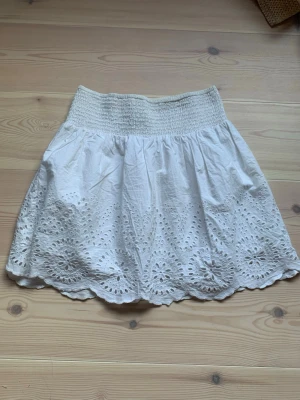 Vit kortkjol med broderade detaljer - Supersöt vit kortkjol från Cubus i storlek XS. Kjolen har bred resår i midjan och fina broderade hålmönster längs hela nederkanten. Tillverkad i bomull och har en enkel design för sommarens alla dagar