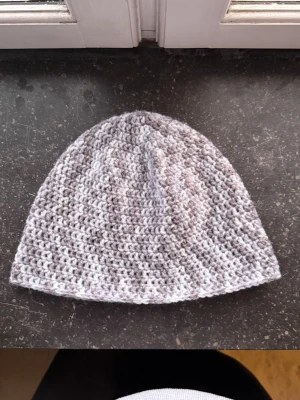 Grå virkad mössa - Säljer en virkad mössa i gråmelerad färg. Mössan är virkad med ett grovt garn som ger en snygg struktur och passar perfekt för kyliga dagar. Enkel och stilren design som funkar till de flesta outfits.
