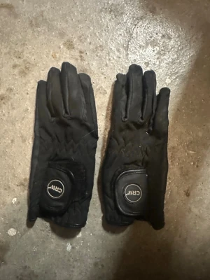 Svarta ridvantar från CRW - Säljer ett par svarta ridvantar från CRW med förstärkta partier i handflatan och justerbar kardborre vid handleden. Vantarna är tillverkade i ett slitstarkt material som ger bra grepp och komfort när du rider.