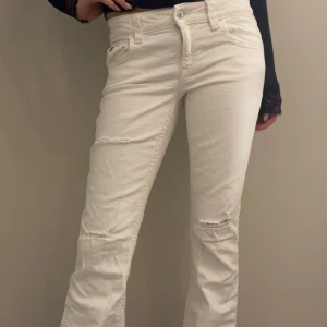 Vita raka jeans med slitningar - Säljer ett par vita jeans med bootcut ben och snygga slitningar vid knäna. Byxorna har klassisk femficksdesign, normal passform och är tillverkade i bomull. Perfekta för dig som vill ha en clean men ändå edgy look.