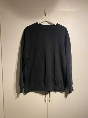 Svart oversized sweatshirt - En svart oversized sweatshirt med rund hals och långa ärmar. Tröjan har ribbade muddar vid ärmslut och nederkant samt dragsko längst ner för justerbar passform. Storlek S och true to size. Välanvänd men i okej skick. 
