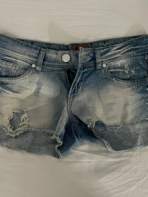 Coola lågmidjade jeansshorts  - Säljer ett par blå jeansshorts med slitna detaljer och fransig kant. Shortsen har klassisk femficksmodell, knapp och dragkedja framtill samt coola slitningar och tvättade partier för en avslappnad look.Shortsen är klippta med till🩷Passar xs/s kanske även m💓