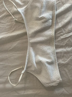 Vit strukturerad väst från H&M - Säljer en vit väst från H&M i storlek 40. Västen har smala axelband och ett strukturerat tyg med vågig yta. Materialet är polyester och elastan vilket gör den stretchig och bekväm. Perfekt för dig som gillar enkel men snygg stil.