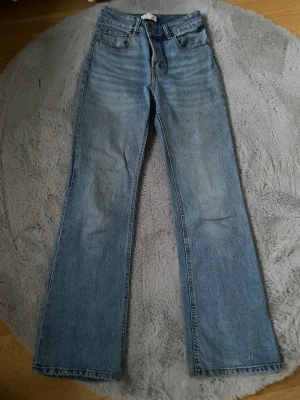 Blå raka jeans från H&M - Säljer ett par klassiska blå jeans från H&M och hög midja. Jeansen har knäppning med fyra silverfärgade knappar och femficksmodell. Materialet är slitstark bomullsdenim i en ljusblå tvätt. Perfekta till sneakers eller boots.