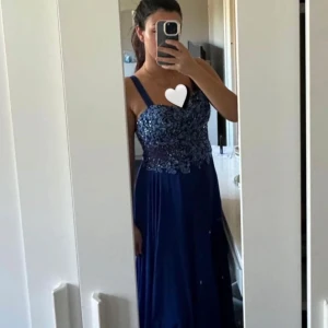 Blå långklänning med paljetter - Säljer en elegant blå långklänning med glittriga paljetter och broderier upptill. Klänningen har breda axelband och en flytande kjol i lätt material. Perfekt för bal eller festliga tillfällen. Snygg och klassisk modell som ger en lyxig känsla.                        Passar en S eller M i storlek. 