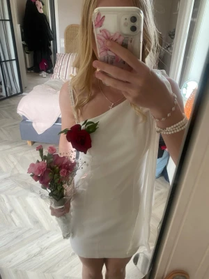 Vit klänning - Vit klänning som är ganska kort, använd en gång under konfirmation och rosen på bilden var fastnålad  och är inte kvar/ ingen del av klänningen. Den är one shoulder och har rosett över axeln💞 För mer bilder skriv privat ❤️Passar perfekt till student eller konfirmation.
