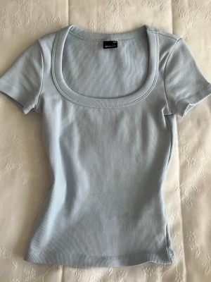 Ljusblå ribbad topp från Gina Tricot - Supersöt ljusblå ribbad topp från Gina Tricot med korta ärmar och urringning. Sitter tight, mjuk och stretchig i materialet. 