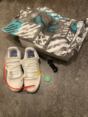 Nike x Off-White Presto - Nike x Off-White Presto sneakers i vitt mesh med gula och orange detaljer, ikonisk Off-White text och zip-tie. Skorna har snörning, platt sula och extra svarta skosnören. Snygg och unik design med genomskinliga plastdetaljer och AIR-tryck på hälen. Äkta från Stock X, verifieringstagg kommer, Röd tagg samt box kommer. Kan definitivt sänka vid snabb försäljning.