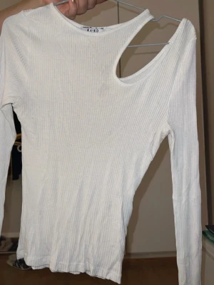 Ribbad tajt tröja - Trendig vit ribbad topp från NA-KD med lång ärm och unik oneshoulder-design. Toppen har en smal passform och är tillverkad i mjuk bomullsmix som känns skön mot huden. Perfekt för dig som gillar stilrena plagg med en twist.