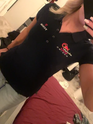 Mörkblå Red Bull Racing piké - Säljer en mörkblå pikétröja från Red Bull Racing med broderade loggor och detaljer i rött, vitt och gult. Tröjan har krage, knappar framtill och korta ärmar. Perfekt för dig som gillar motorsport och vill ha en sportig look.