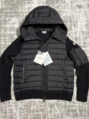 Svart cardigan från Moncler - Säljer en svart cardiga från Moncler med stickade ärmar och huva. Jackan har dragkedja framtill, två fickor med knapp och en extra ficka på ärmen. Perfekt för dig som vill ha en snygg och sportig look i vinter.