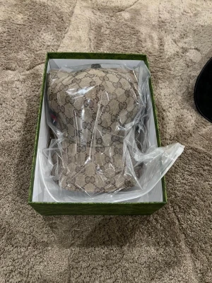 Beige keps med monogram - Säljer en beige keps med det klassiska monogrammönstret över hela plagget. Västen har en stilren och tidlös design som sticker ut med sitt exklusiva märke. Perfekt för dig som vill ha något unikt och trendigt i garderoben.